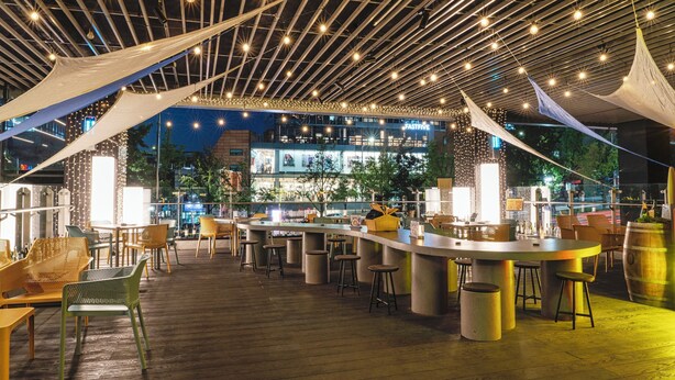 An outdoor bar area with a wooden floor, multiple seating options including chairs and stools, and a bar counter. - voco Seoul Gangnam by IHG (Seoul)