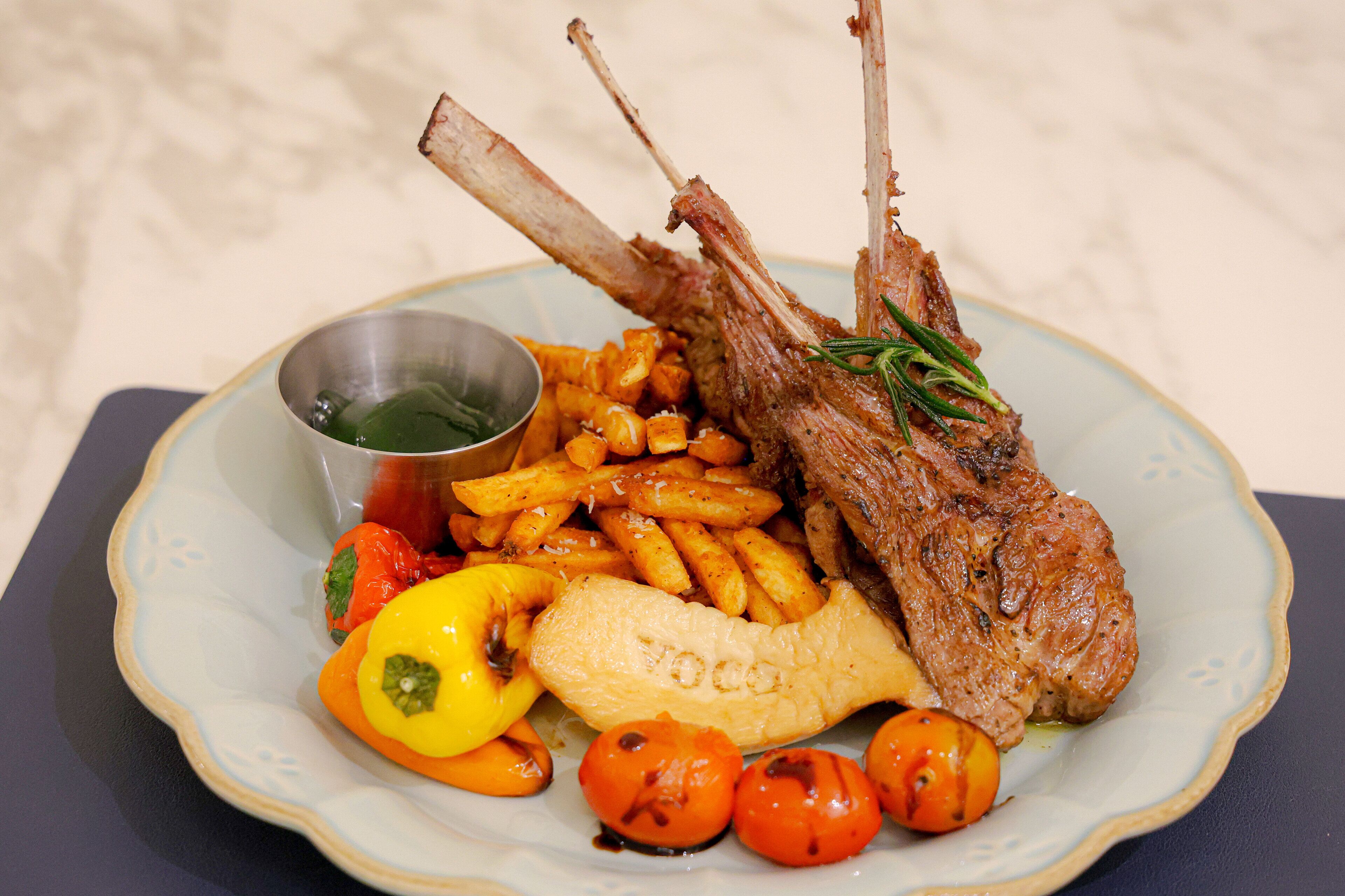 A plate with roasted lamb chops, fries, and roasted vegetables.