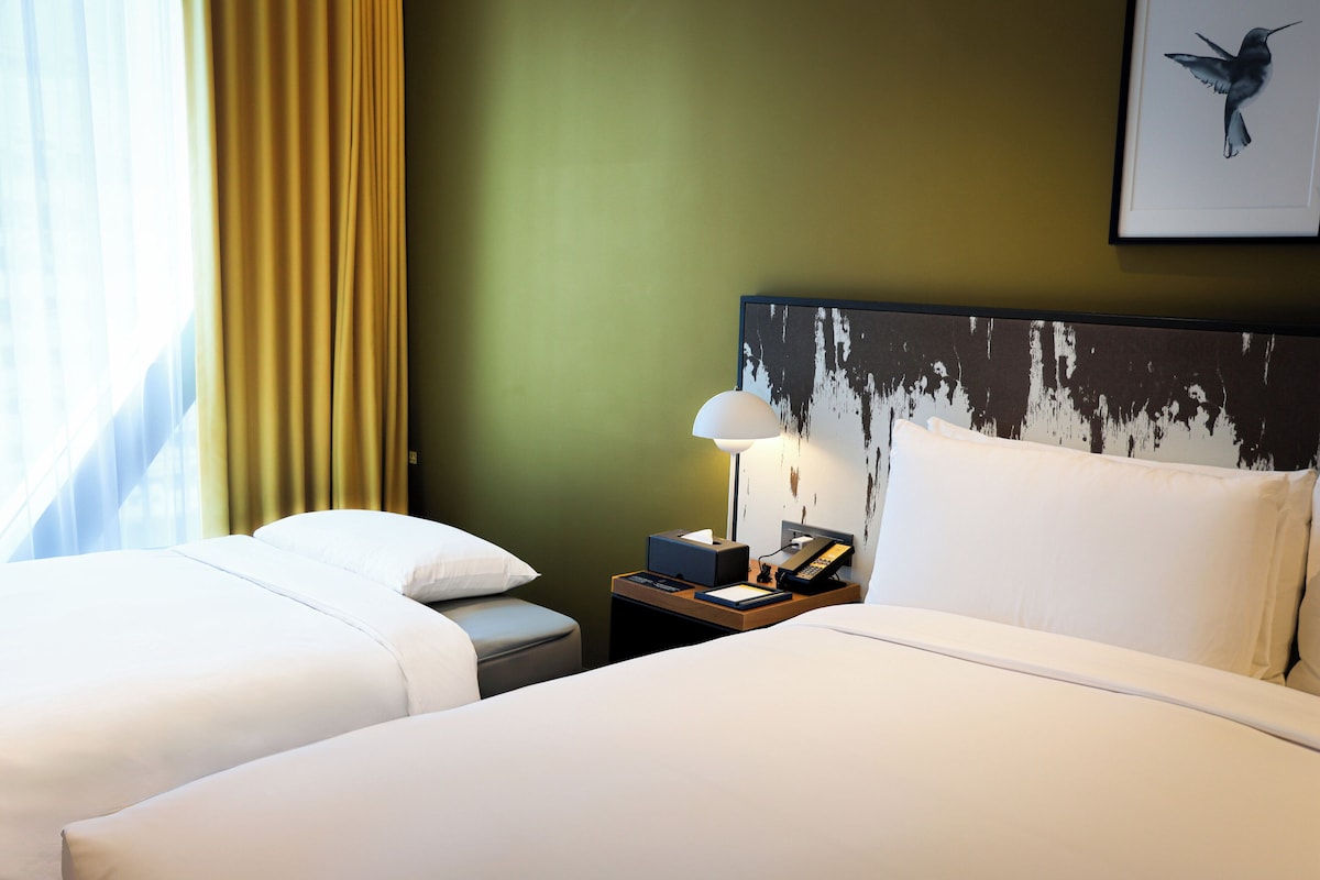 A hotel room with two beds, a nightstand with a lamp, a telephone, and a framed picture on the wall.