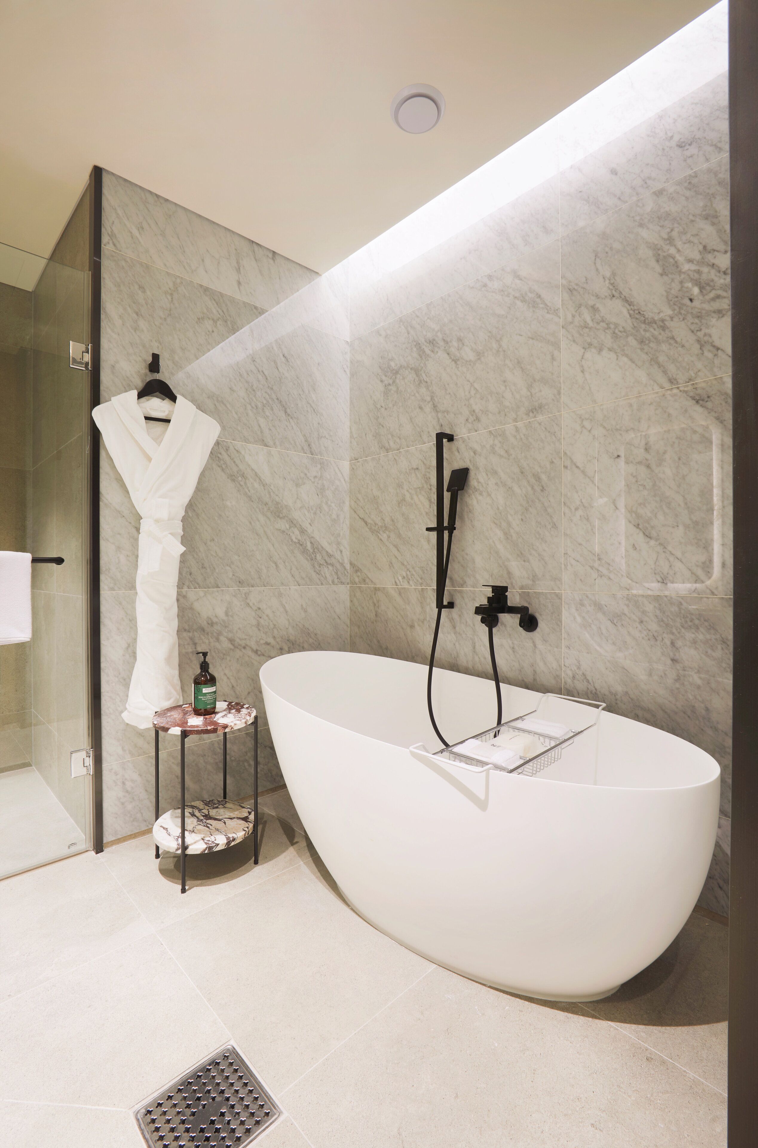 Un baño moderno con una bañera independiente, cabina de ducha con mampara de cristal y un perchero con bata blanca.