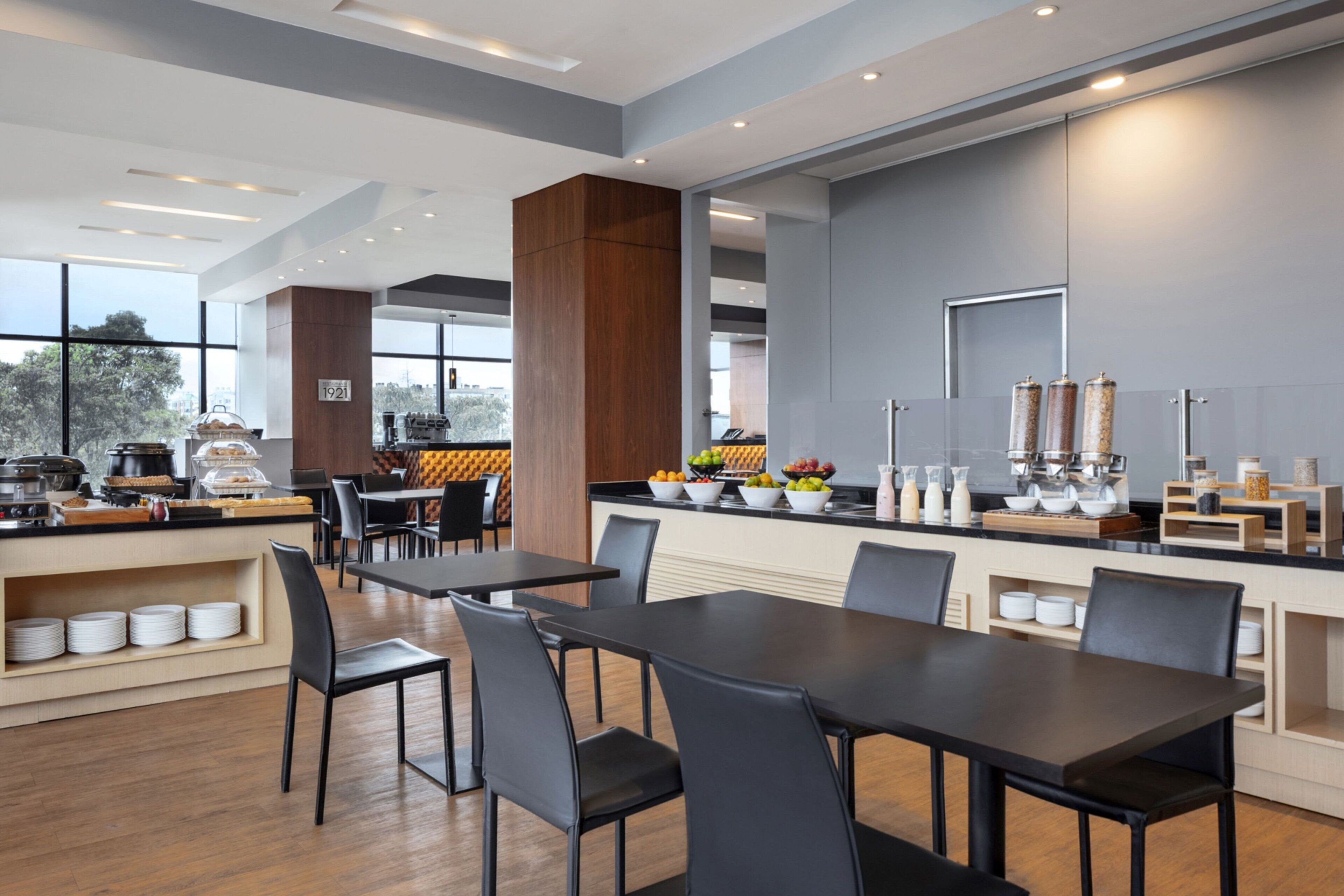 A modern dining area with a long counter, black chairs, and a variety of food items displayed.