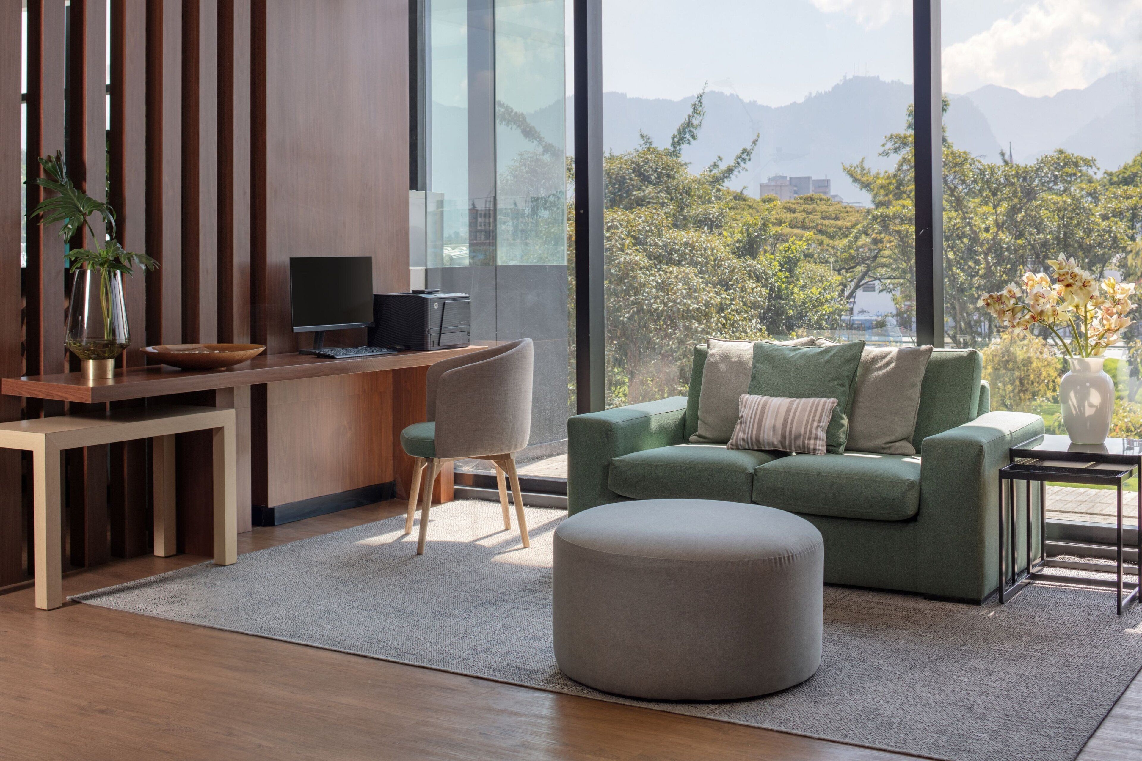 Een moderne woonkamer met een bureau, een groene bank en uitzicht op bergen.