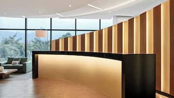 Un área de recepción moderna con un mostrador curvo, ventanas amplias que ofrecen vistas a árboles y montañas, y un sofá con una mesita de centro.