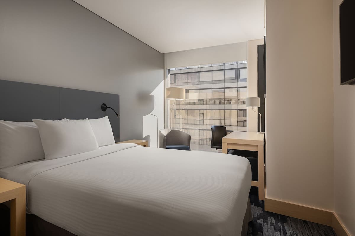 A hotel room with a large bed, a desk, a chair, and a TV.