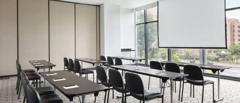 Un salón de conferencias con una gran pantalla de proyección, varias mesas y sillas.