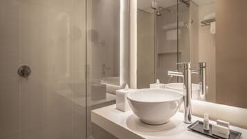Un baño moderno con un lavamanos grande de color blanco, una cabina de ducha de vidrio y un espejo que refleja el ambiente.