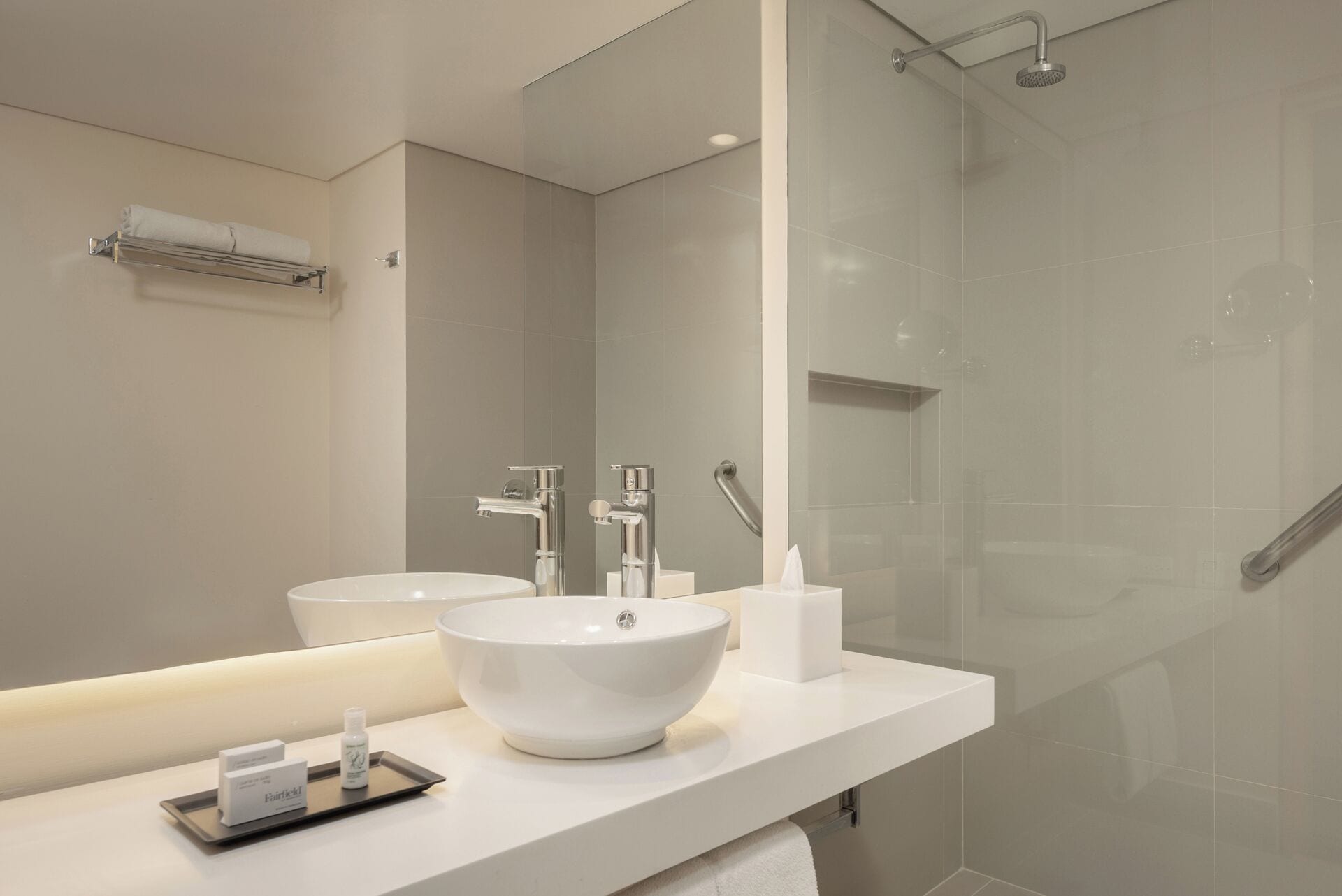 Un baño moderno con un espejo grande, dos lavamanos, una ducha y un perchero para toallas.