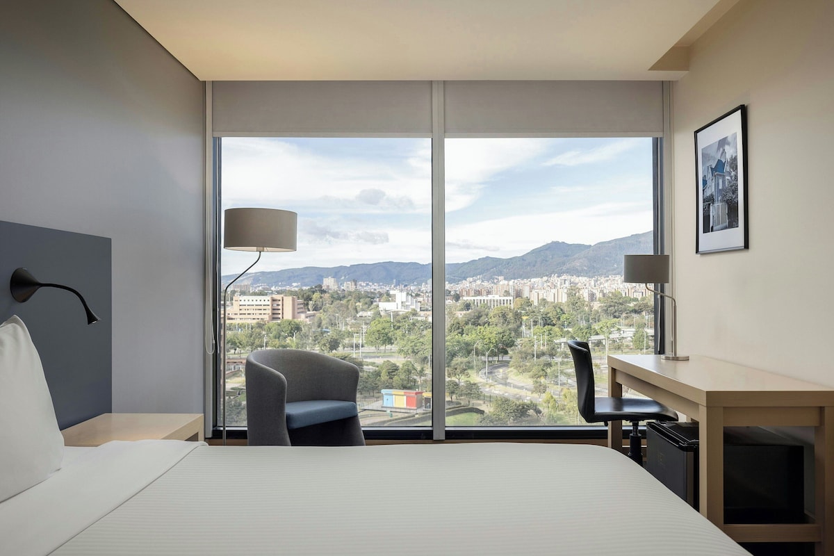 Habitación de hotel con una ventana grande, cama, escritorio y silla.