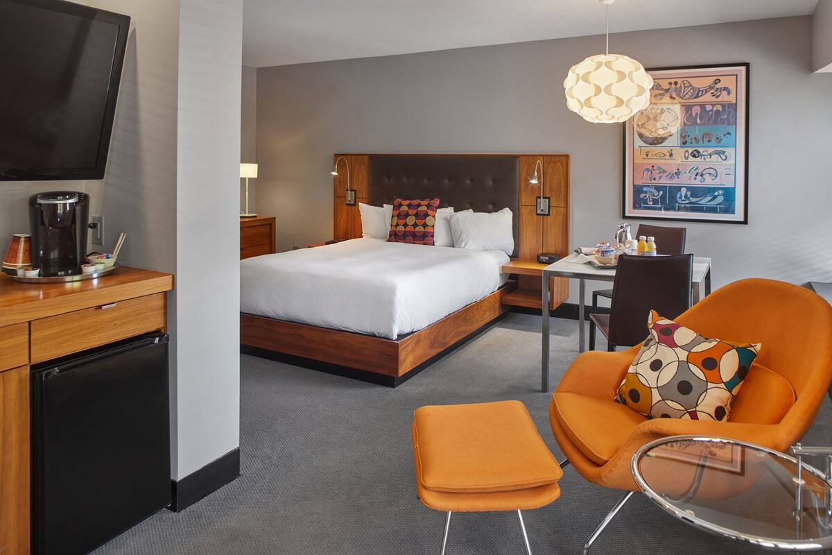 A hotel room with a bed, a desk, a chair, a coffee machine, and a TV.
