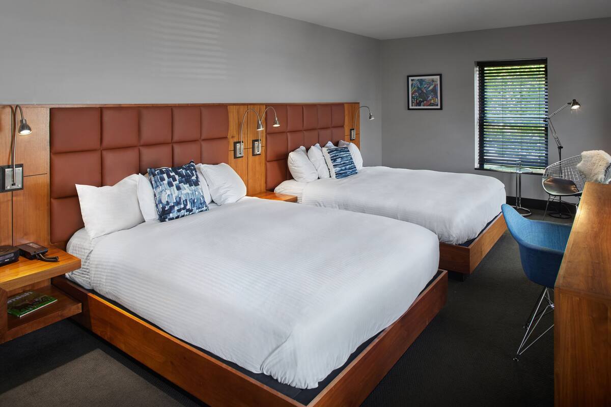 A hotel room with two beds, wooden headboards, bedside lamps, a desk, and a chair.