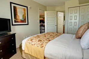 Un dormitorio ordenado con una cama, un televisor sobre una cómoda y un cuadro en la pared.