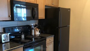 A kitchen with wooden cabinets, a black microwave, a black refrigerator, a stove, and a stainless steel sink. - Clearwater Residence Hotel Timberlea (Fort McMurray)
