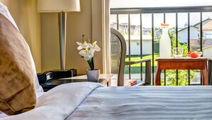 A hotel room with a bed, a desk with a lamp, a chair, a potted orchid, and a balcony with a view of houses. - Clearwater Residence Hotel Timberlea (Fort McMurray)