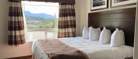 Ein Hotelzimmer mit einem großen Bett, Blick auf Berge durch das Fenster und zwei gerahmte Bilder an der Wand.