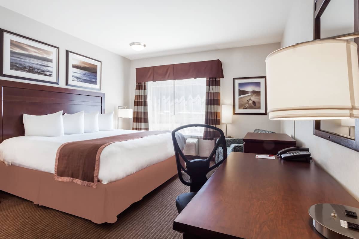 Una habitación de hotel con una cama grande, un escritorio, una silla, un teléfono y una ventana con cortinas.
