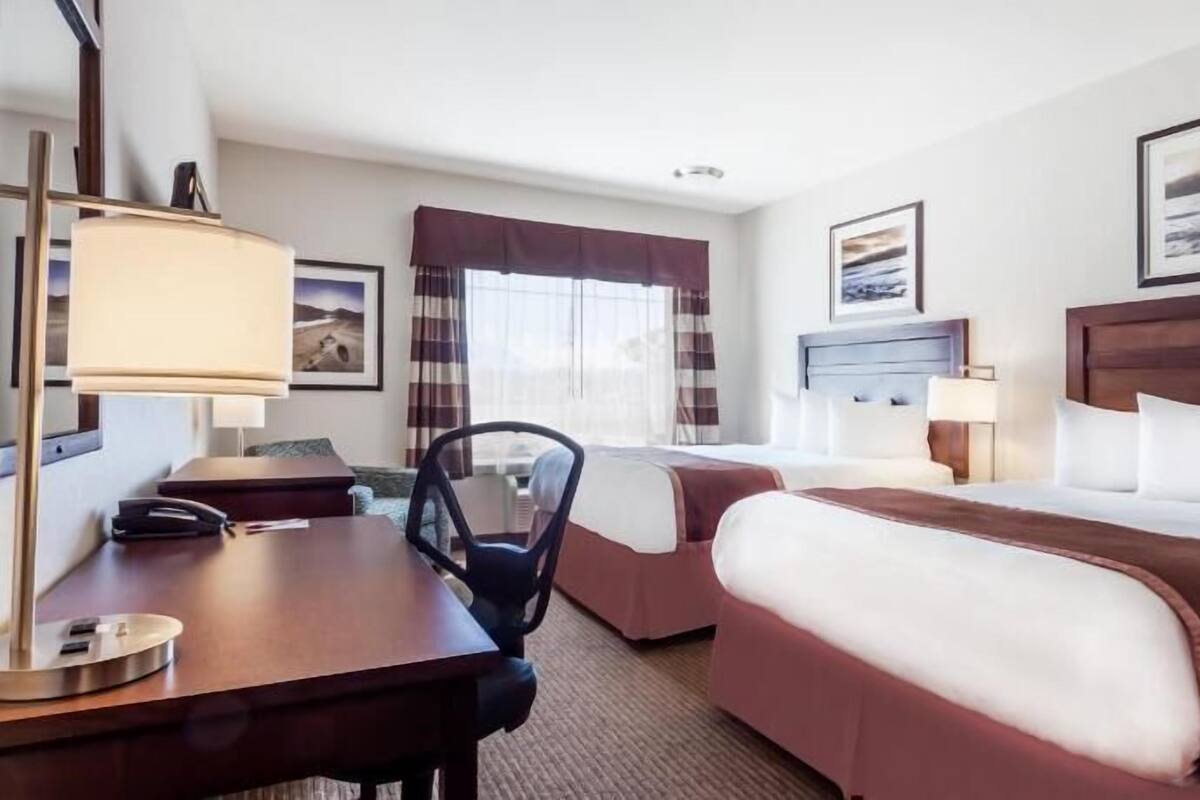 Habitación de hotel con dos camas, un escritorio, una silla, una lámpara y una ventana con cortinas.