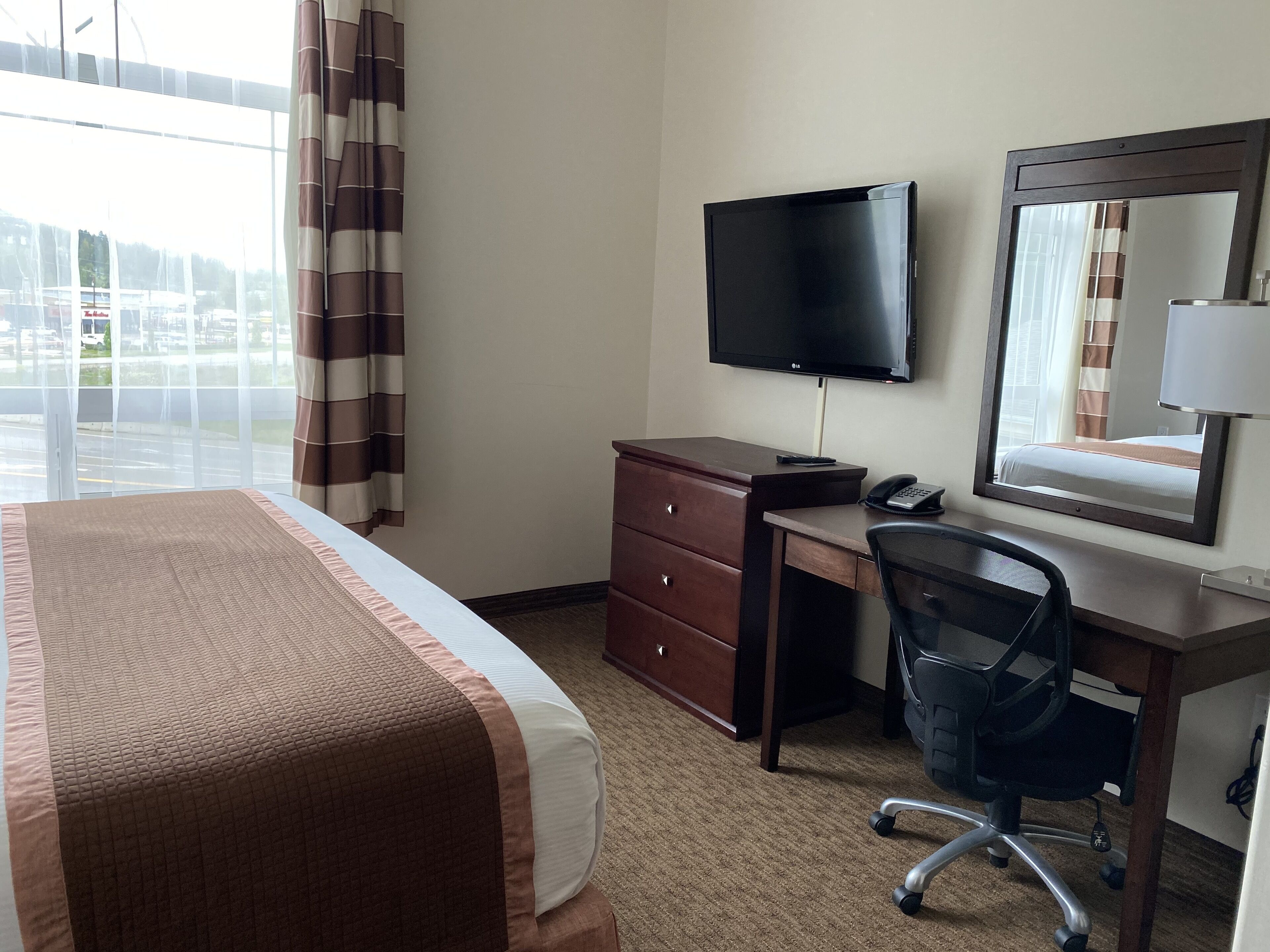 Une chambre d’hôtel comprenant un lit, un bureau avec une chaise, un téléviseur à écran plat, un téléphone et un miroir.