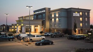 Un hotel de diseño moderno, con una entrada destacada con columnas y un letrero que dice "Chateau Inn & Suites". Se observan varios espacios de estacionamiento, y el edificio está iluminado por luces exteriores.