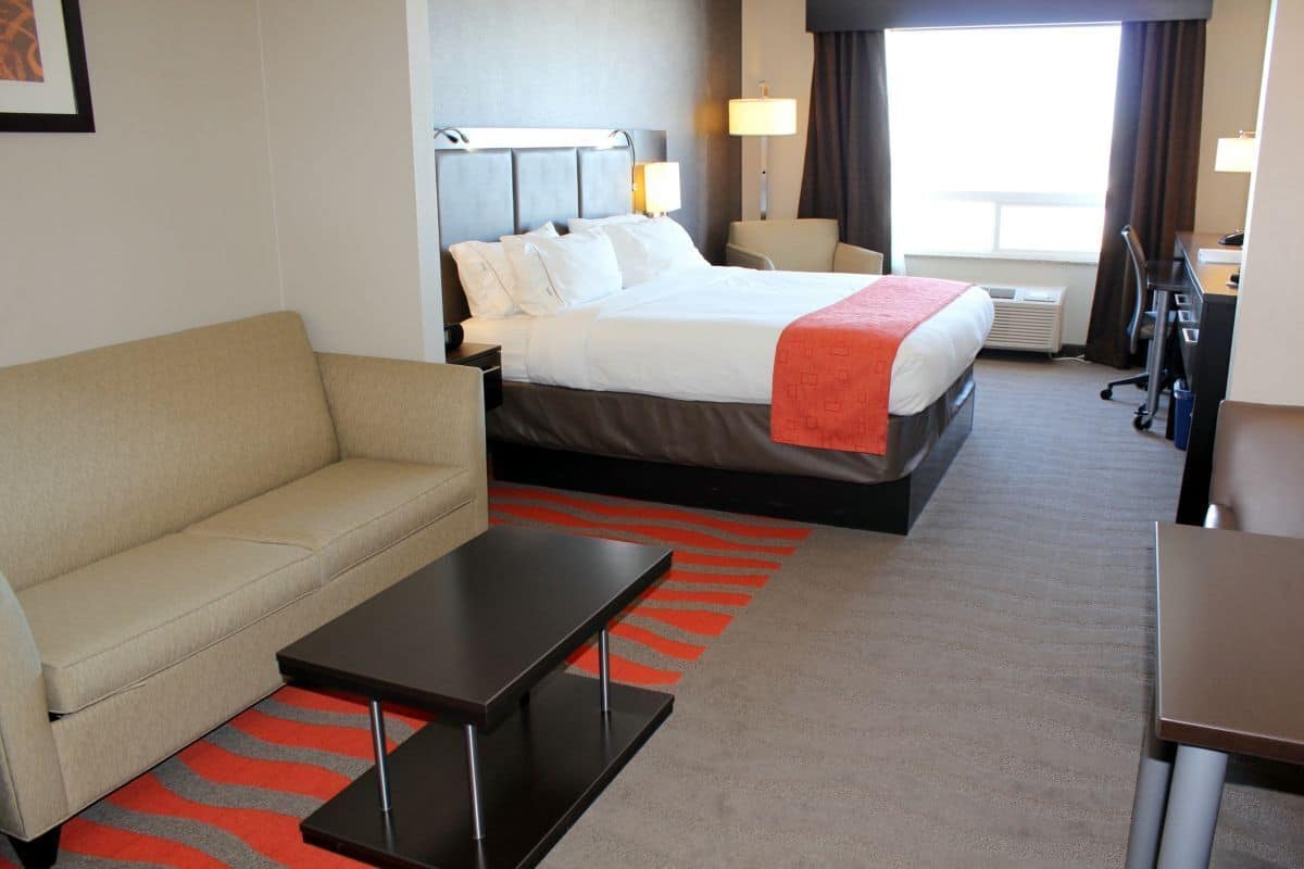 Habitación de hotel con cama, sofá, escritorio y lámpara, y vistas al exterior.