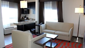 Una habitación de hotel con kitchenette, un sofá, una mesita y una lámpara de pie.