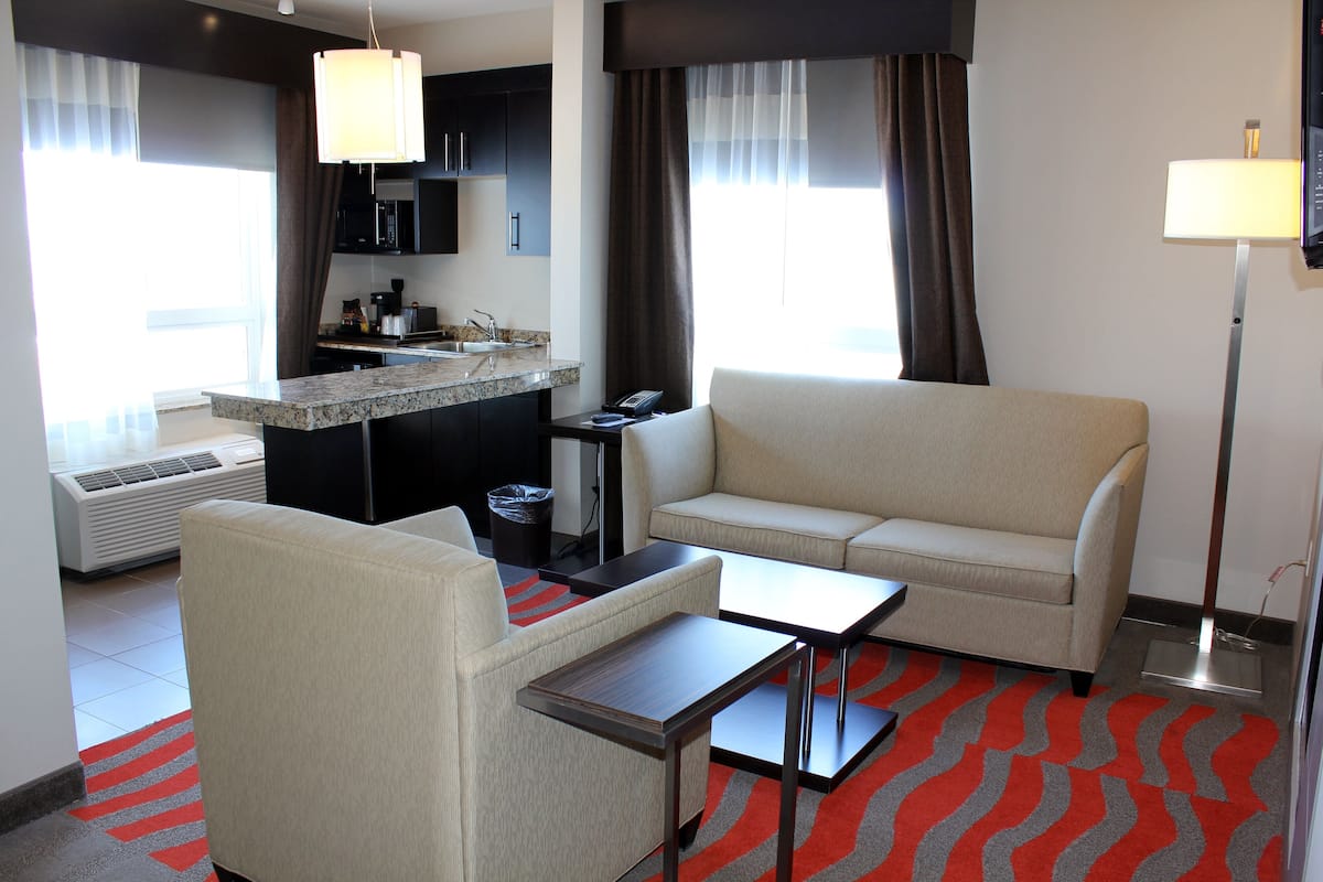 Una habitación de hotel con kitchenette, un sofá, una mesita y una lámpara de pie.