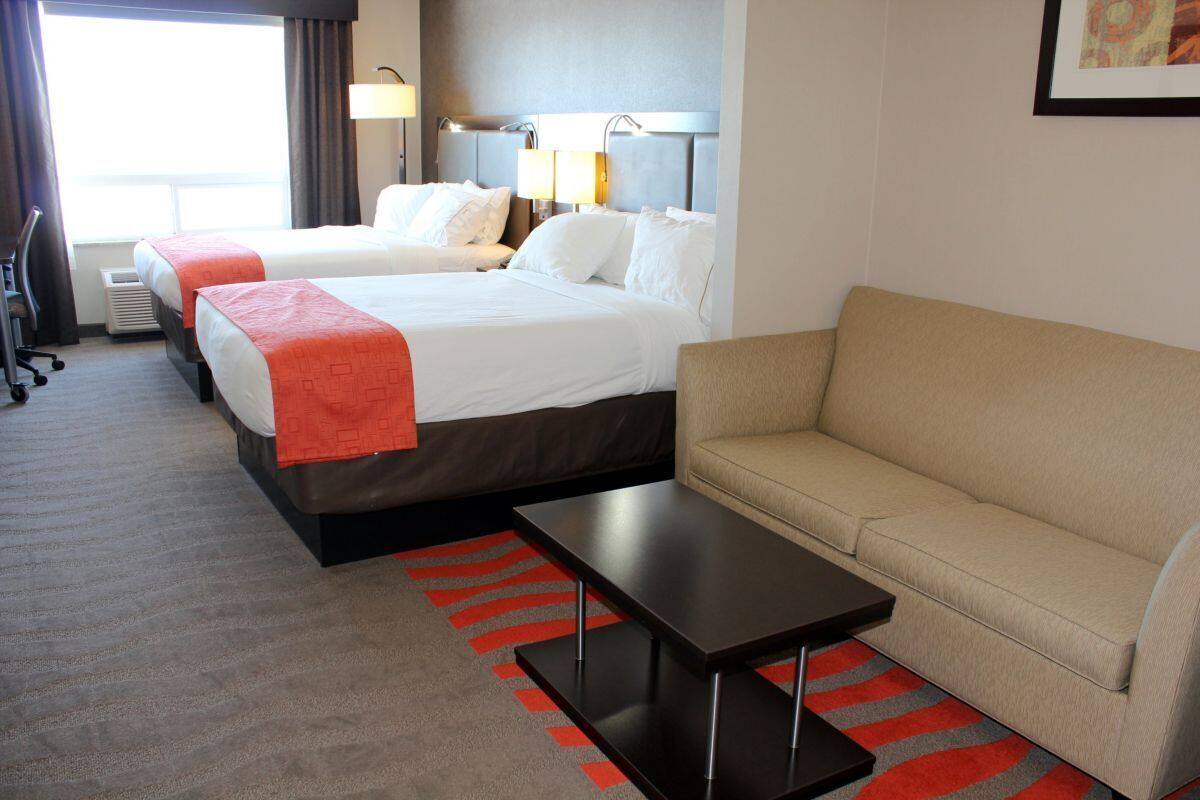 Habitación de hotel con dos camas, un sofá, una mesa de centro y vistas al exterior.