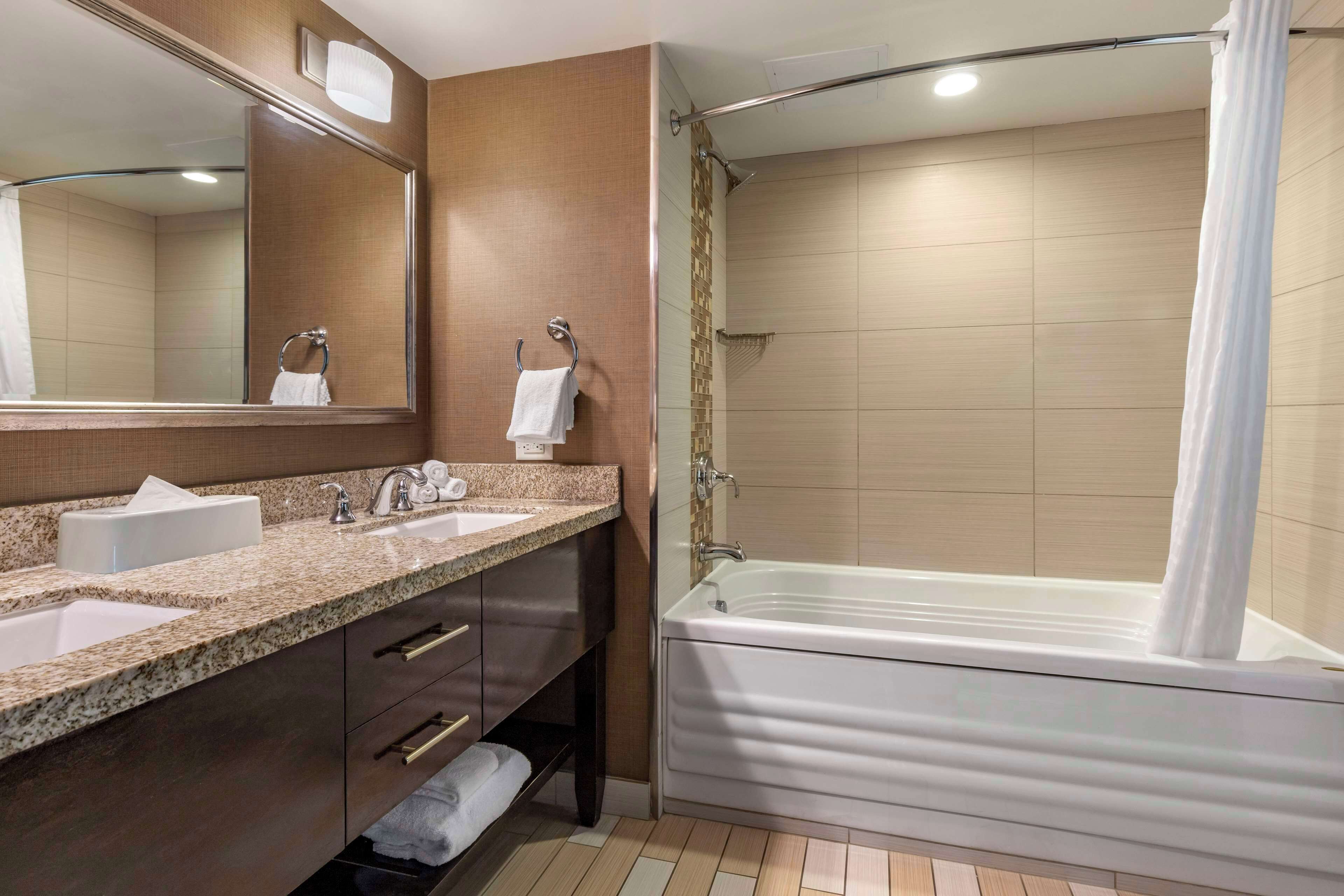 A bathroom with two sinks, a large mirror, a bathtub, and a shower curtain.