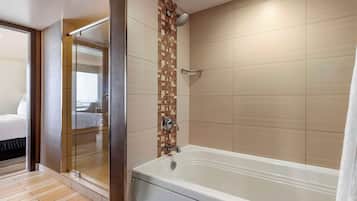 Un baño moderno con ducha acristalada, una bañera amplia y una pared de azulejos con diseño tipo mosaico.