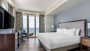 Una habitación de hotel moderna con una cama grande, un televisor de pantalla plana, un escritorio y vistas al mar a través de amplios ventanales.