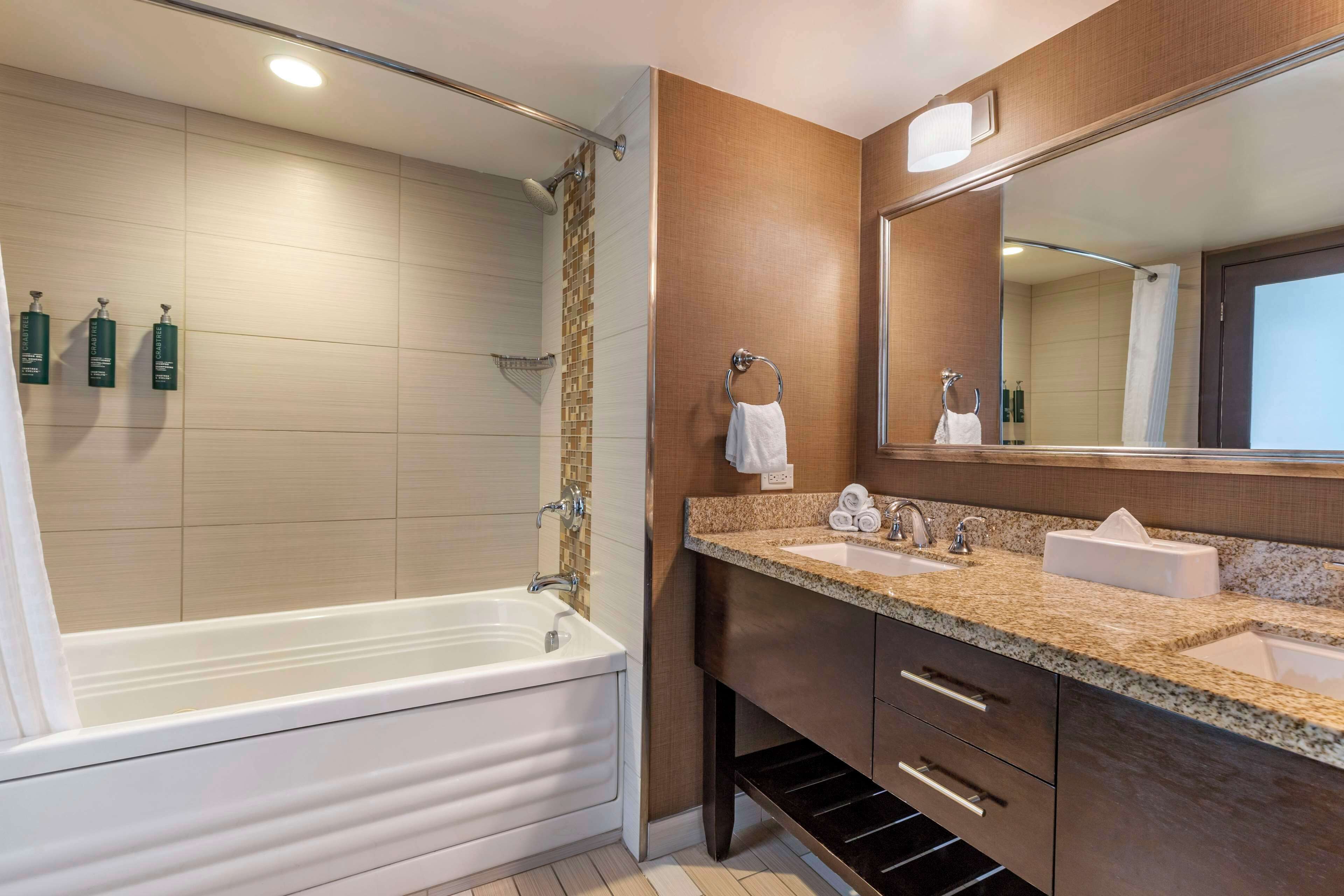 A modern bathroom with a bathtub, two sinks, a large mirror, and a towel rack.