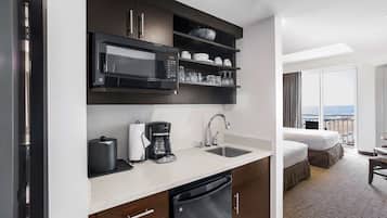 Una cocina de hotel con microondas, cafetera y lavaplatos. Hay una cama y un balcón con vistas.