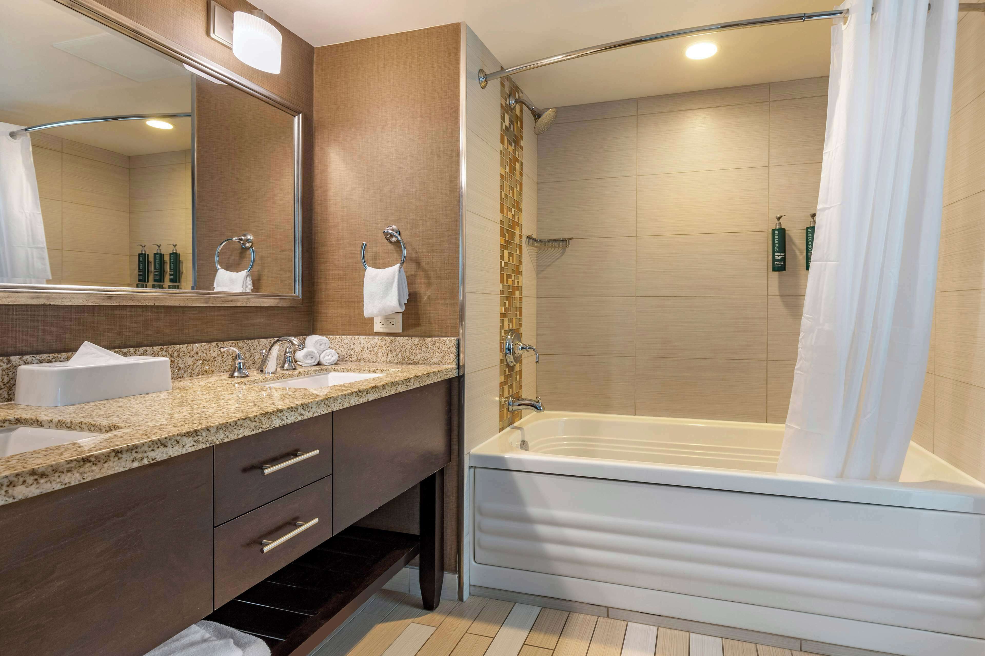 A modern bathroom with a large mirror, two sinks, a bathtub, and a shower.