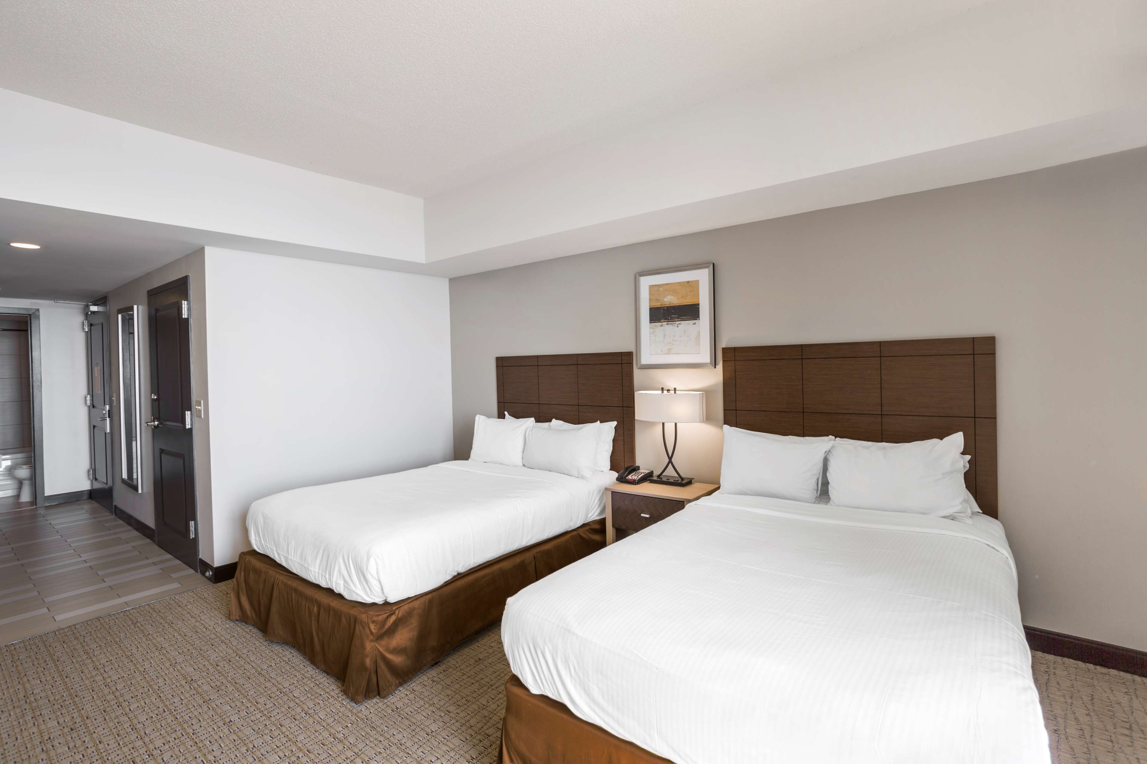 A hotel room with two beds, a nightstand, a lamp, and a framed picture on the wall.