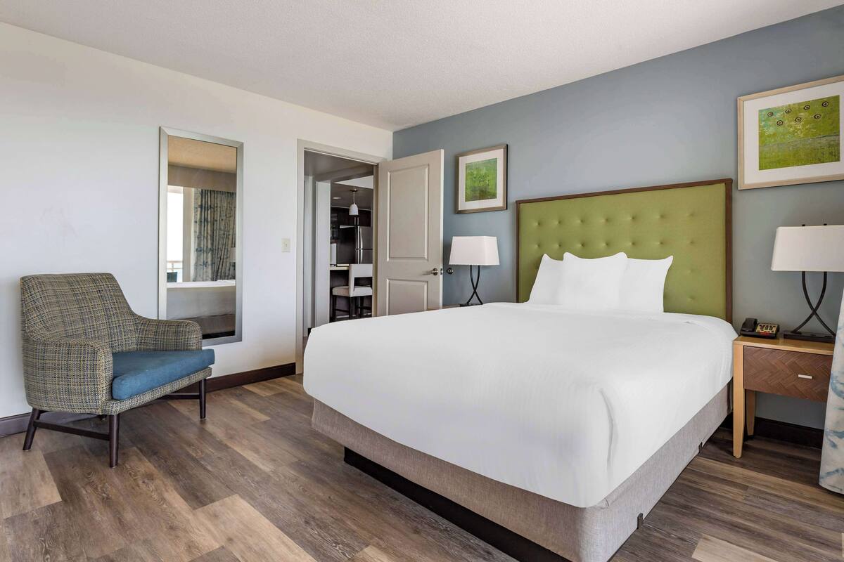 A hotel room with a large bed, a chair, a nightstand, and a door leading to a bathroom.