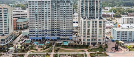 A high-rise hotel with multiple floors, a swimming pool, landscaped gardens, and a statue.