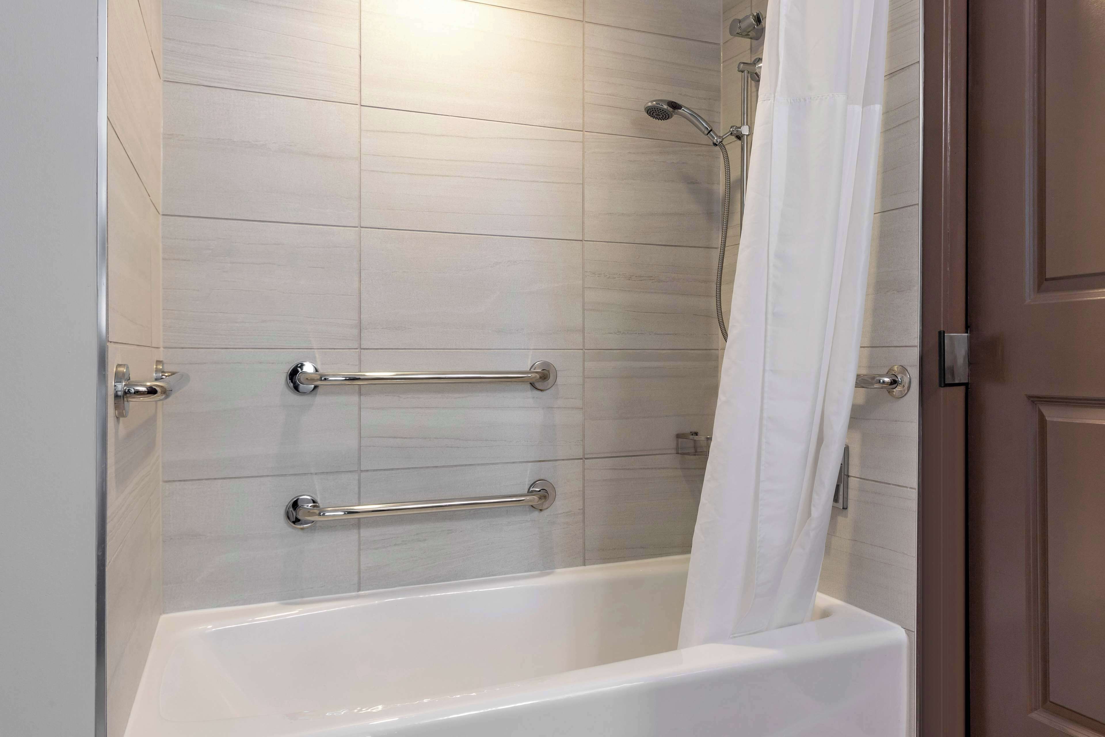 A modern bathroom with a white bathtub, grab bars, and a showerhead.