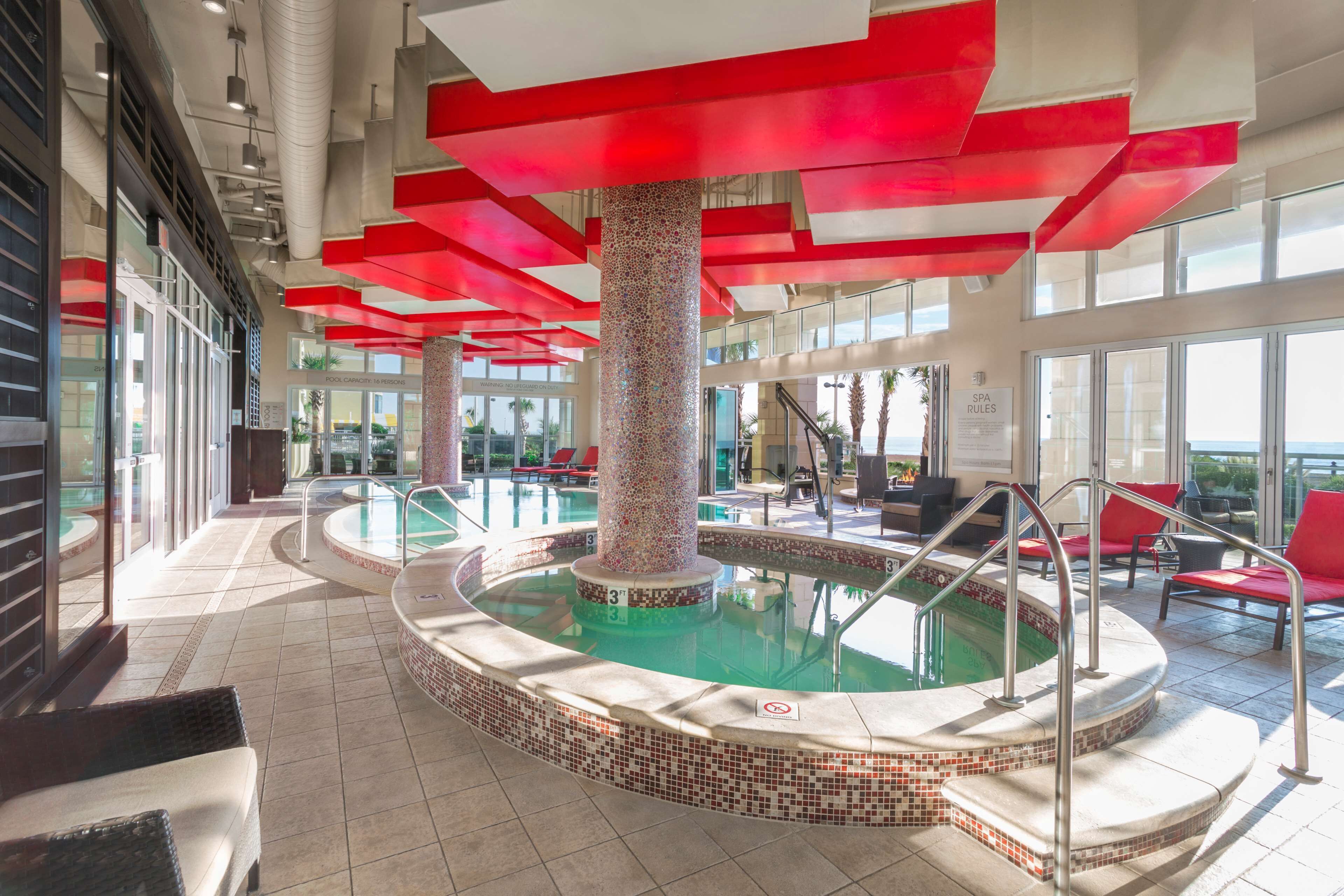 A pool area with red accents, a central pillar, and a view of the ocean.