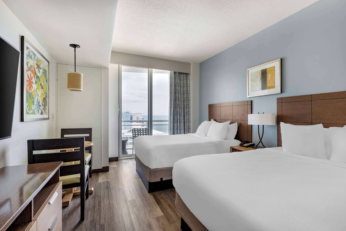 A hotel room with two beds, a desk, and a chair.