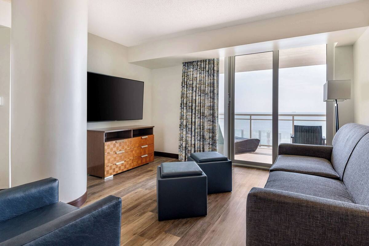 A modern living room with a flat-screen TV, a sofa, ottomans, and a wooden cabinet.