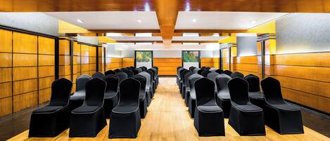 Une salle de conférence avec des rangées de chaises noires et des murs recouverts de panneaux en bois.