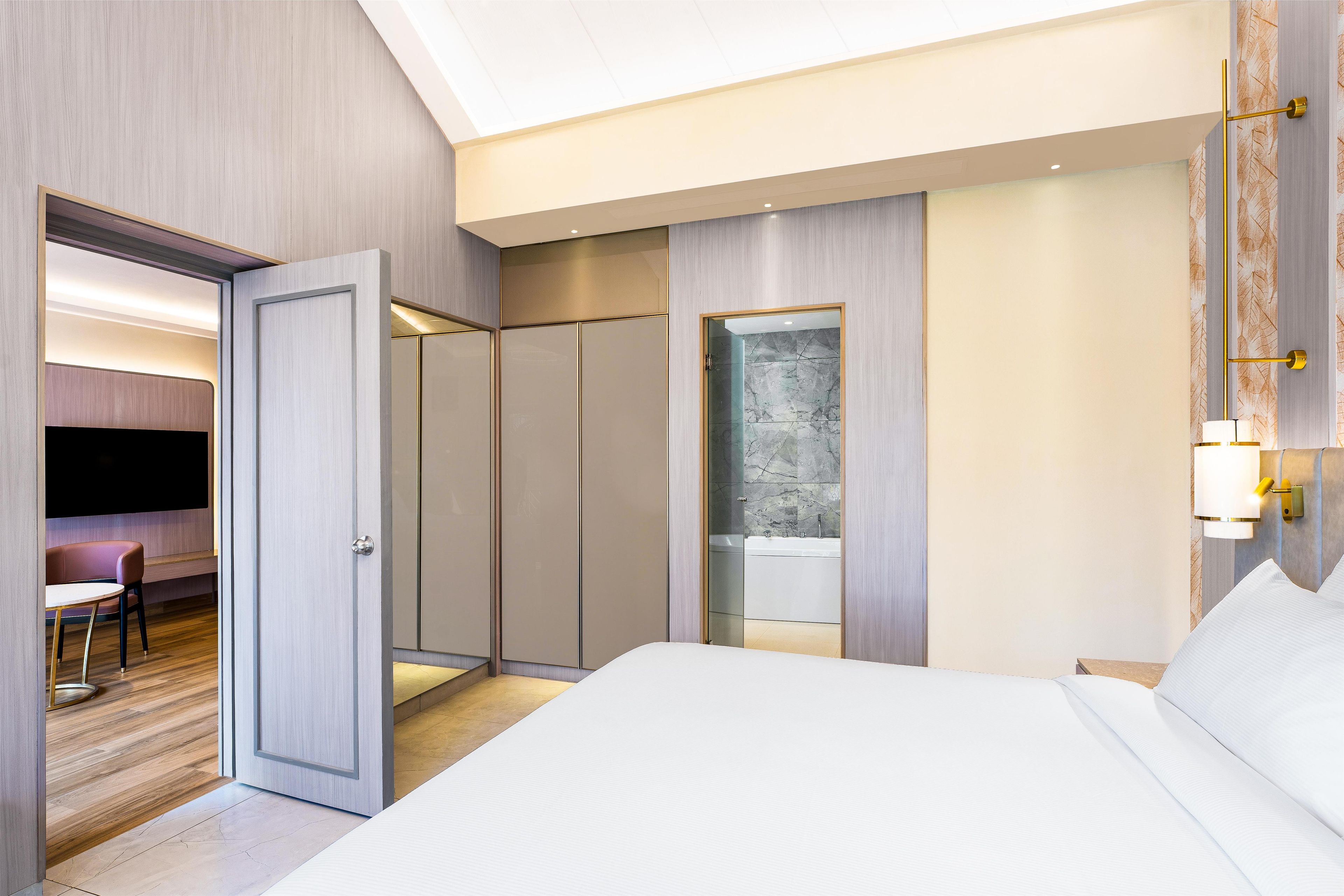 Une chambre d’hôtel moderne dotée d’un grand lit, d’un coin salon avec un fauteuil, d’une armoire et d’une salle de bain avec baignoire.