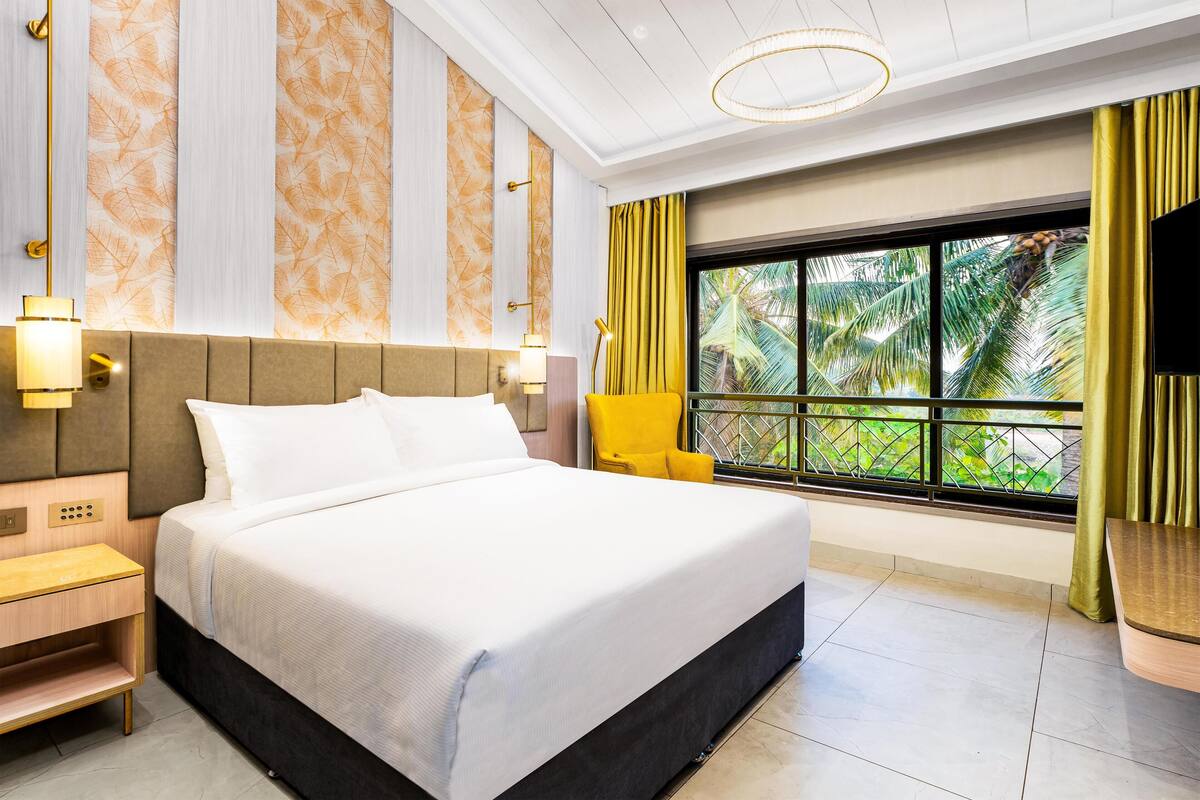 A hotel room with a large bed, a nightstand, a chair, a TV, and a window with curtains.