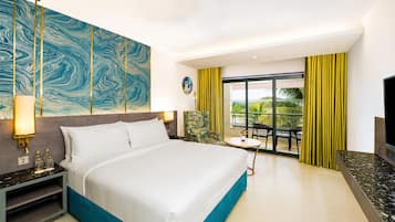 Habitación de hotel con una cama grande, una mesita de noche, una lámpara, un televisor y vistas al exterior a través de un ventanal.