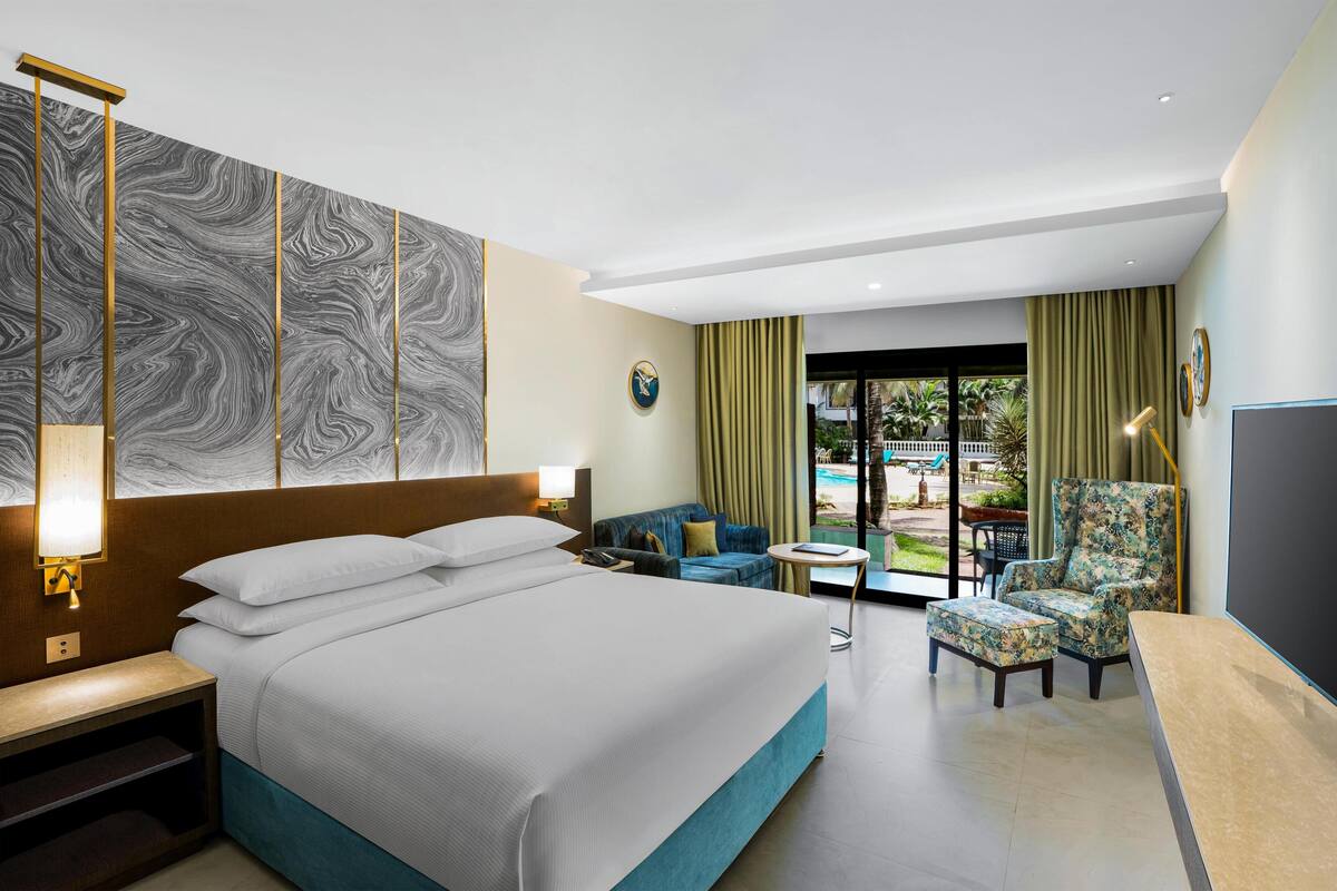 A hotel room with a large bed, a sofa, a chair, a small table, and a view of the outdoors.