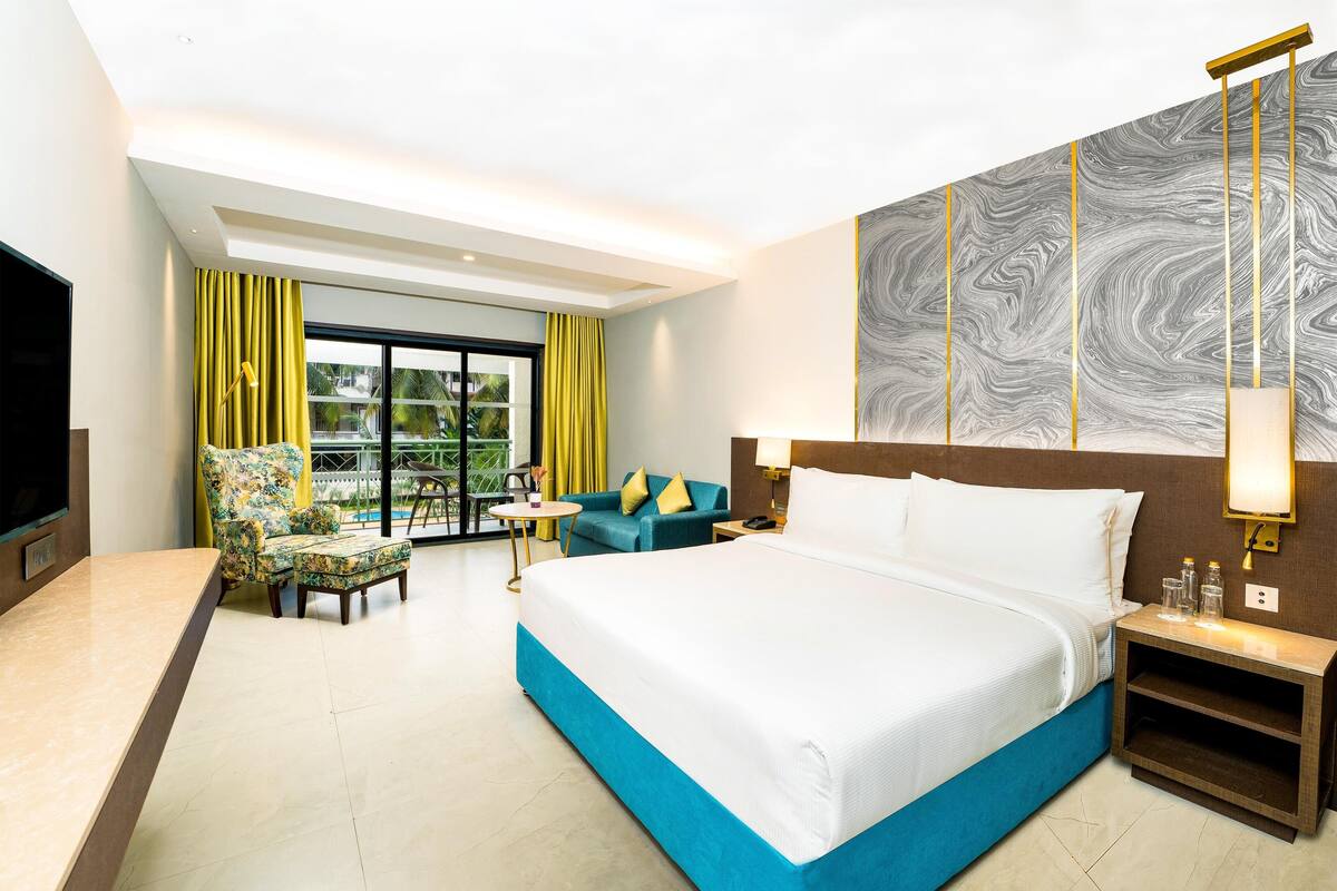 A hotel room with a large bed, a desk, a chair, a sofa, a TV, and a window with curtains.