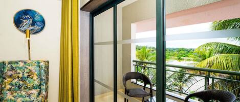 A balcony with a view of a green landscape, a chair, a table, and a wall-mounted lamp.