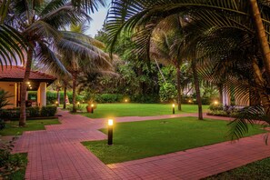 A pathway leading to a building with a red roof, surrounded by lush greenery and palm trees. - DoubleTree by Hilton Hotel Goa - Arpora - Baga (Arpora)