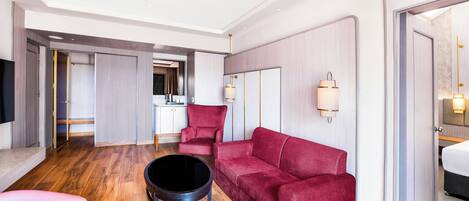 A modern hotel room with a red sofa, a pink chair, a black coffee table, and a TV.