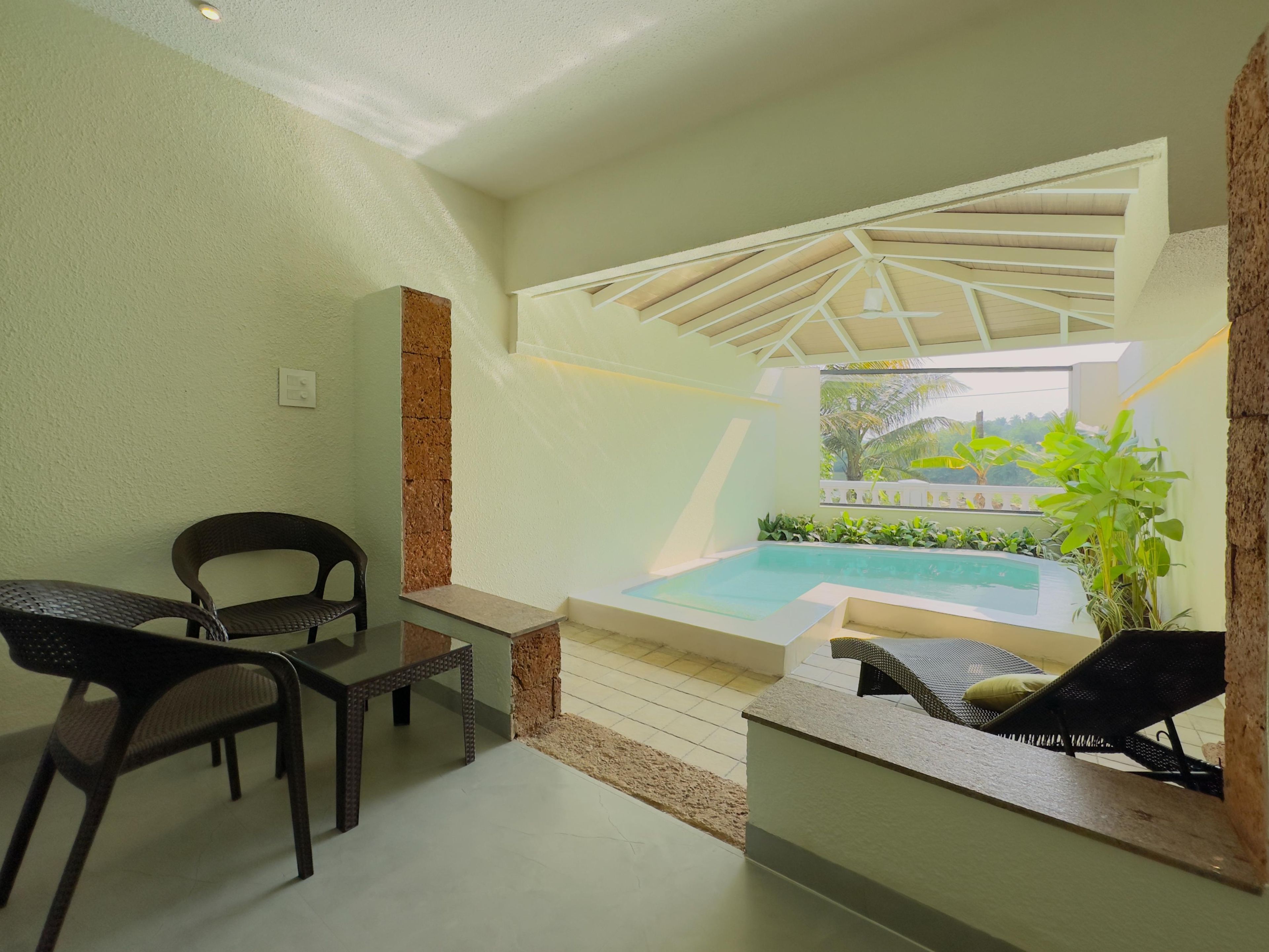 Et lille, afskærmet poolområde med et bord og stole og udsigt til grøn natur, i et simpelt, moderne design.
