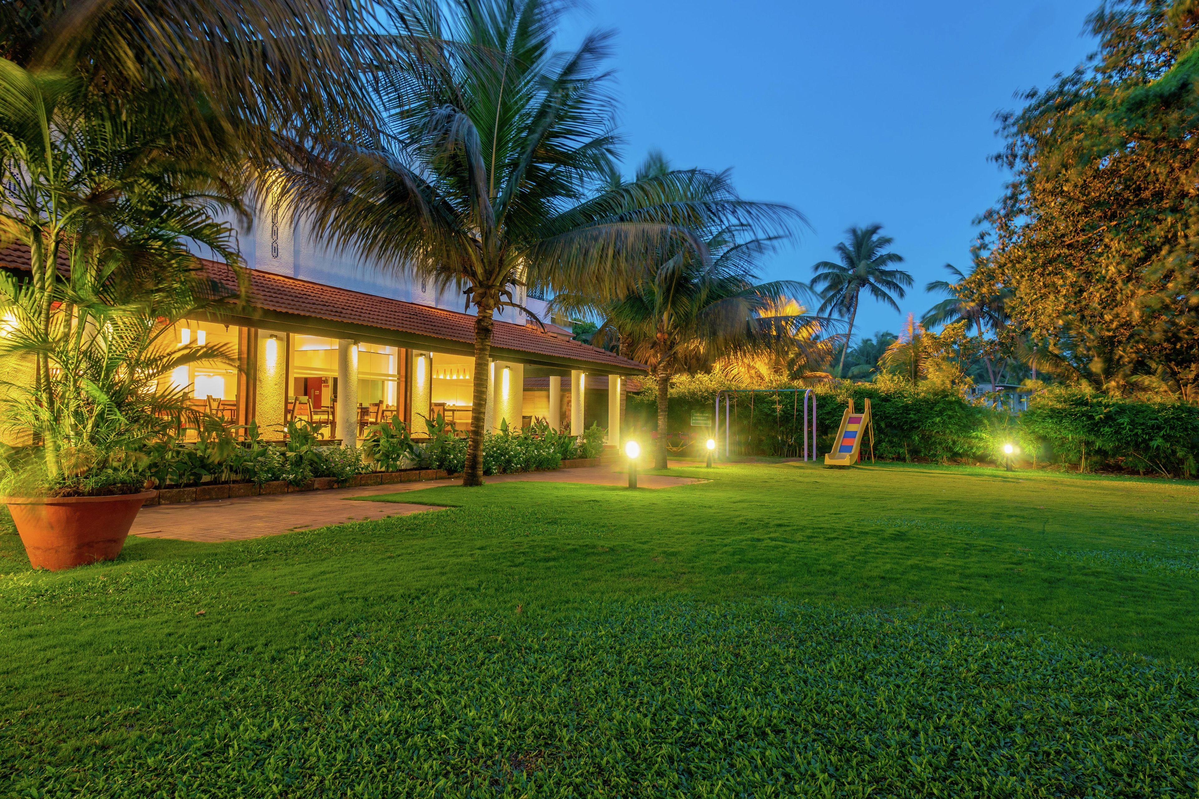 A well-lit building with a red roof, surrounded by lush greenery and palm trees.